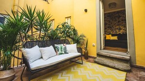 Un bâtiment jaune avec un banc en métal noir et des plantes en pot.