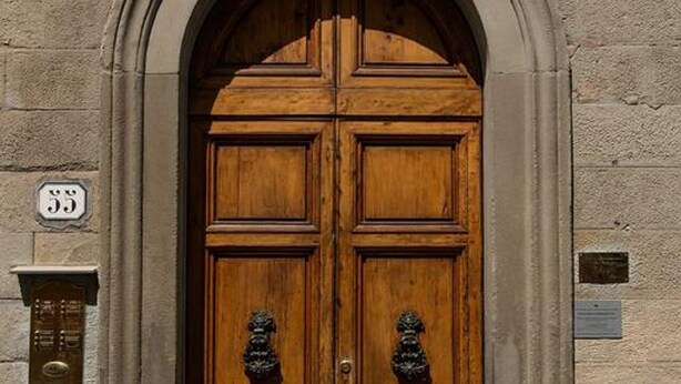 Une porte en bois à deux battants, surmontée d’un arc en pierre, avec une plaque en laiton et un panneau portant le numéro « 55 » fixé au mur.