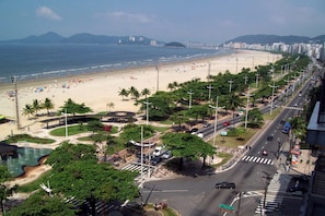 A beach with a road running parallel to it, lined with palm trees and street lamps.