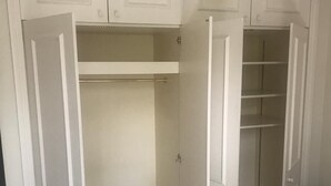 A bedroom with a bed, a wardrobe with open doors, and a closet with shelves. - Beautiful one bedroom in Kensington (London)