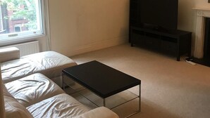 A living room with a sofa, a coffee table, a TV stand, and a fireplace. - Beautiful one bedroom in Kensington (London)