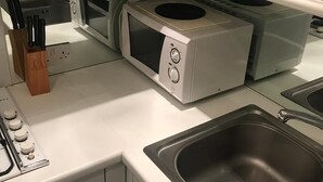 A compact kitchen with a microwave, stove, and sink. There are cabinets with handles and a knife block. - Beautiful one bedroom in Kensington (London)
