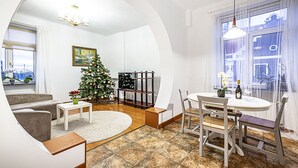 A modern living room with a Christmas tree, a dining table with chairs, a sofa, and a large window with curtains. - WINWINSTAY Residence in Heart of Old Town (Riga)