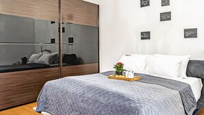 A modern bedroom with a grey quilted bedspread, a wooden bedside table with a tray of lemons and a potted plant, and a large mirror on the wall. - WINWINSTAY Residence in Heart of Old Town (Riga)