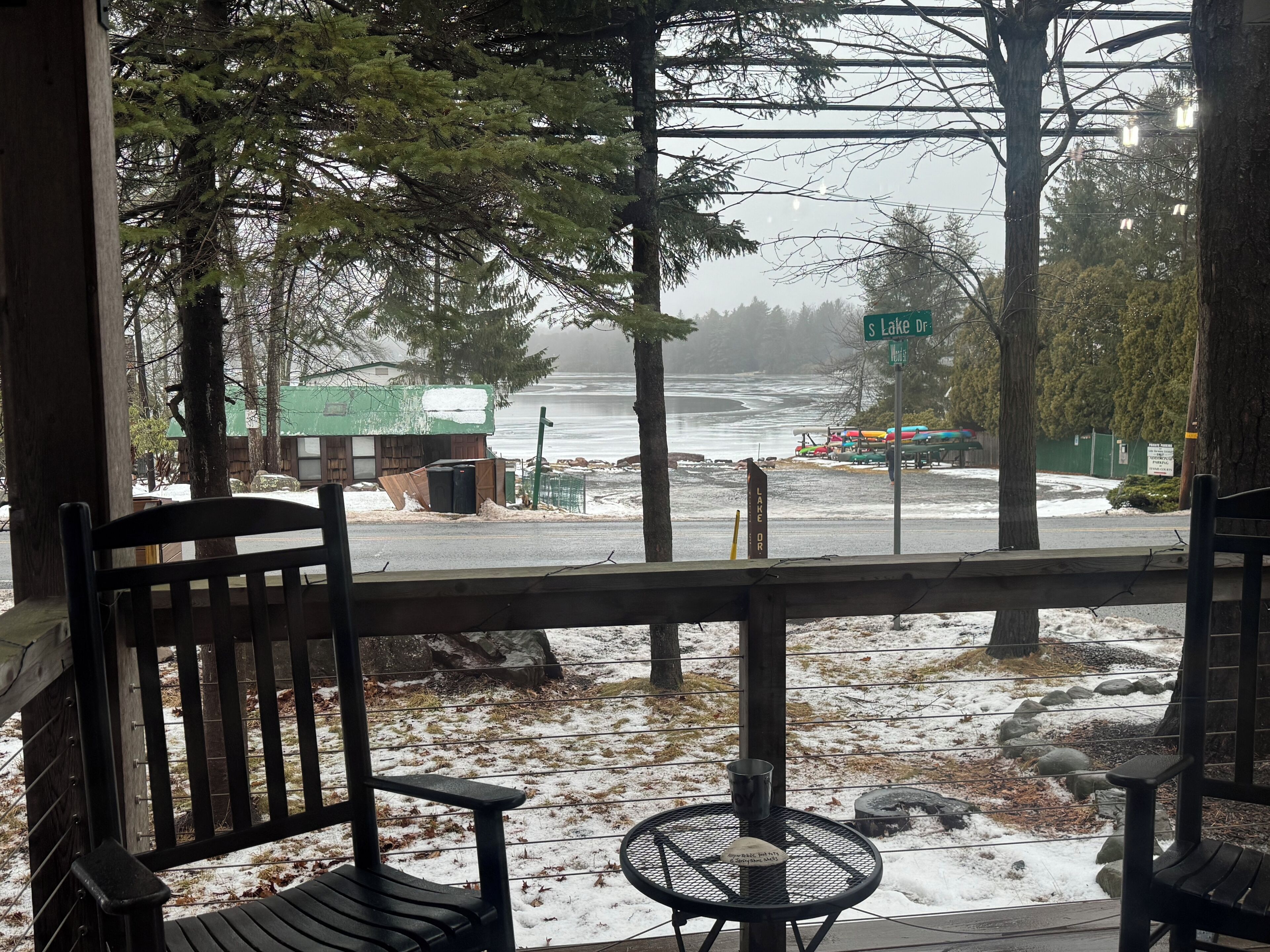A wooden bench and table on a porch overlooking a snowy landscape with a view of a lake and a sign reading "S Lake Dr."