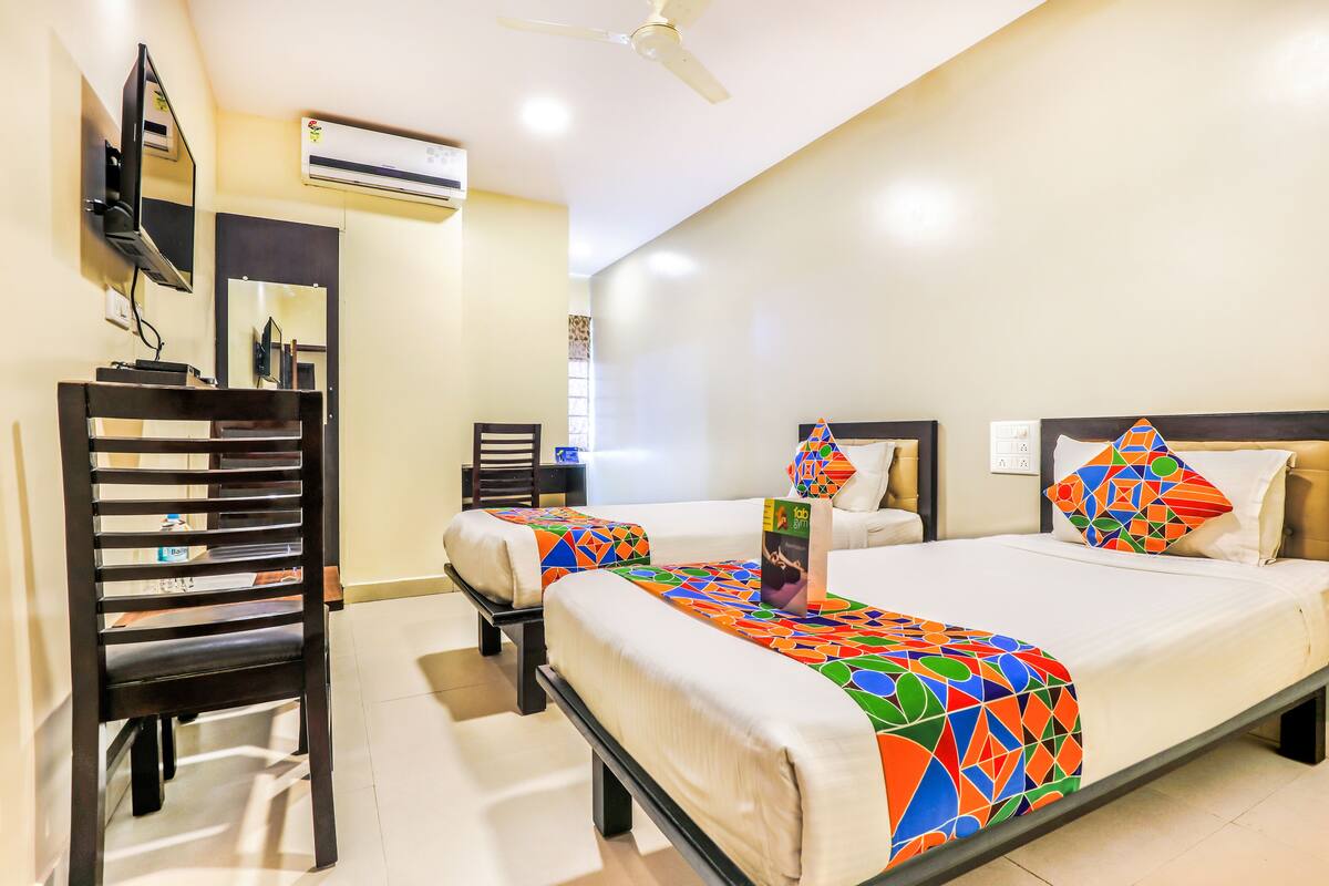 A hotel room with two beds, a TV, and an air conditioning unit.