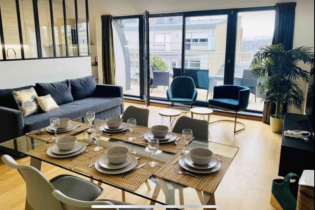 A modern living room with a glass dining table set for four, a sofa, and a balcony with chairs.