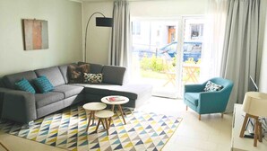 A modern living room with a grey sectional sofa, a teal armchair, a small round table, and a patterned rug. - Large Retro Chic Flat 100m2 in City Center - Parking (Luxembourg City)