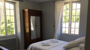 A bedroom with a bed, a wooden wardrobe, a mirror, and two windows with curtains. - Picturesque village,  2 amazing restaurants, creperie and shops a few steps away (Daglan)