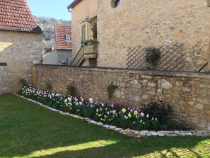 A stone building with a tiled roof, a stone wall with a flower bed, and a grassy area. - Picturesque village, 2 amazing restaurants, creperie and shops a few steps away (Daglan)
