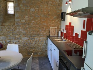 A kitchen with a stone wall, a sink, a stove, and a dining area with a chair and table. - Picturesque village, 2 amazing restaurants, creperie and shops a few steps away (Daglan)