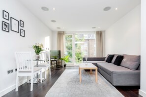 A modern living room with a grey sofa, white chairs, a glass coffee table, and a TV. - Gatliff Road Apartments (London)