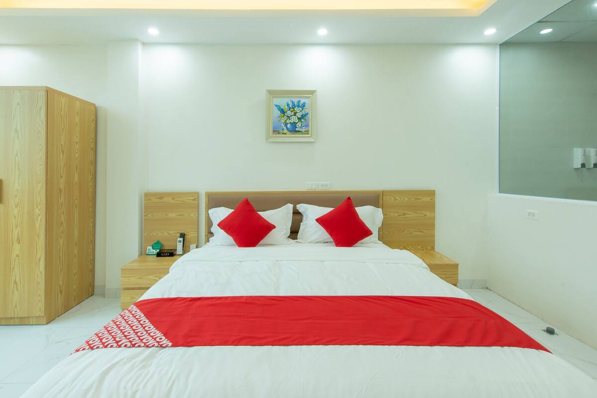 Une chambre d’hôtel moderne avec un grand lit, une tête de lit en bois et une couvre-lit rouge et blanche.