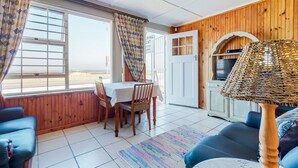 A cozy room with a dining table, chairs, a sofa, a lamp, and a view through a window. - SeaScape Condo (Cape Town)