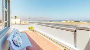 A balcony with a white bench, a potted plant, and a clear view of the ocean and mountains in the distance. - SeaScape Condo (Cape Town)
