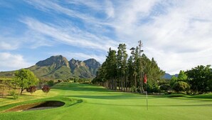 A golf course with a flagstick, trees, and mountains in the background. - SeaScape Condo (Cape Town)