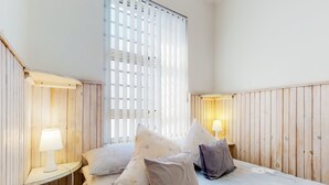 A bedroom with wooden paneling, a bed with floral bedding, and two bedside lamps. - SeaScape Condo (Cape Town)
