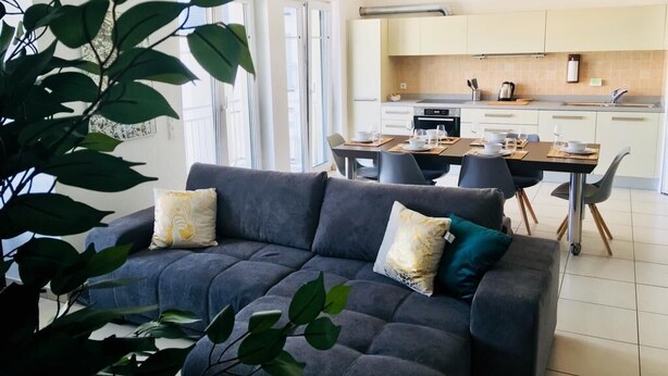 Una sala de estar moderna con un sofá gris, una mesa de comedor con sillas y una cocina al fondo.
