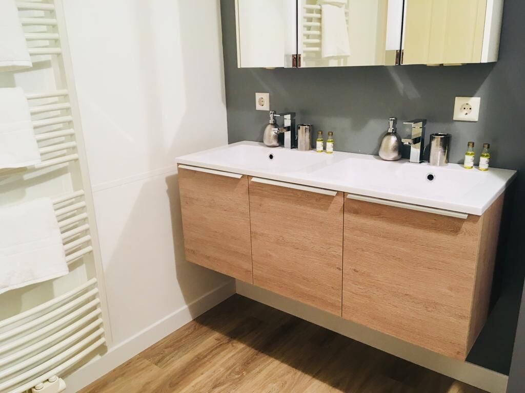 Une salle de bain avec un lavabo blanc, deux miroirs et un meuble en bois.