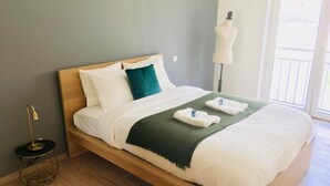 Una cama bien tendida con sábanas blancas, una manta verde y un par de toallas dobladas.
