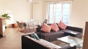 A modern living room with a sofa, a glass coffee table, and a dining area with a glass table and chairs.
