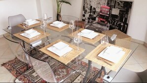 A dining area with a glass table set for six, surrounded by wicker chairs.