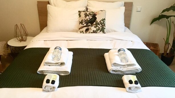 A neatly made bed with white linens, a green bedspread, and two towels with a face design.