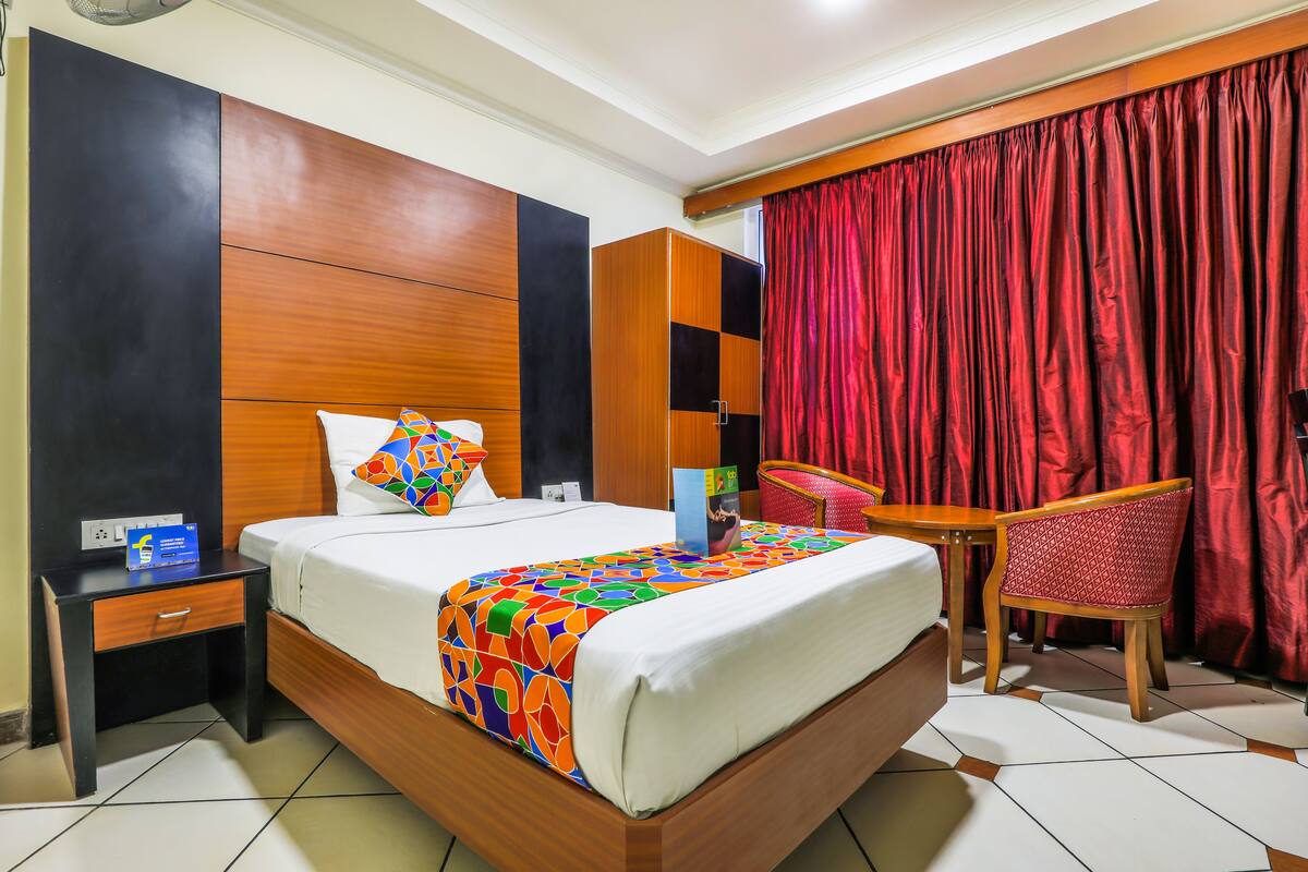 Habitación de hotel con cama, mesita de noche, silla, mesa, armario y cortina roja.