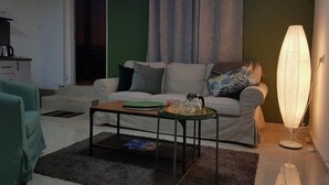 A living room with a sofa, a coffee table, a lamp, and a kitchen area in the background. - Large Beautiful Studio in Old Jaffa (Tel Aviv)