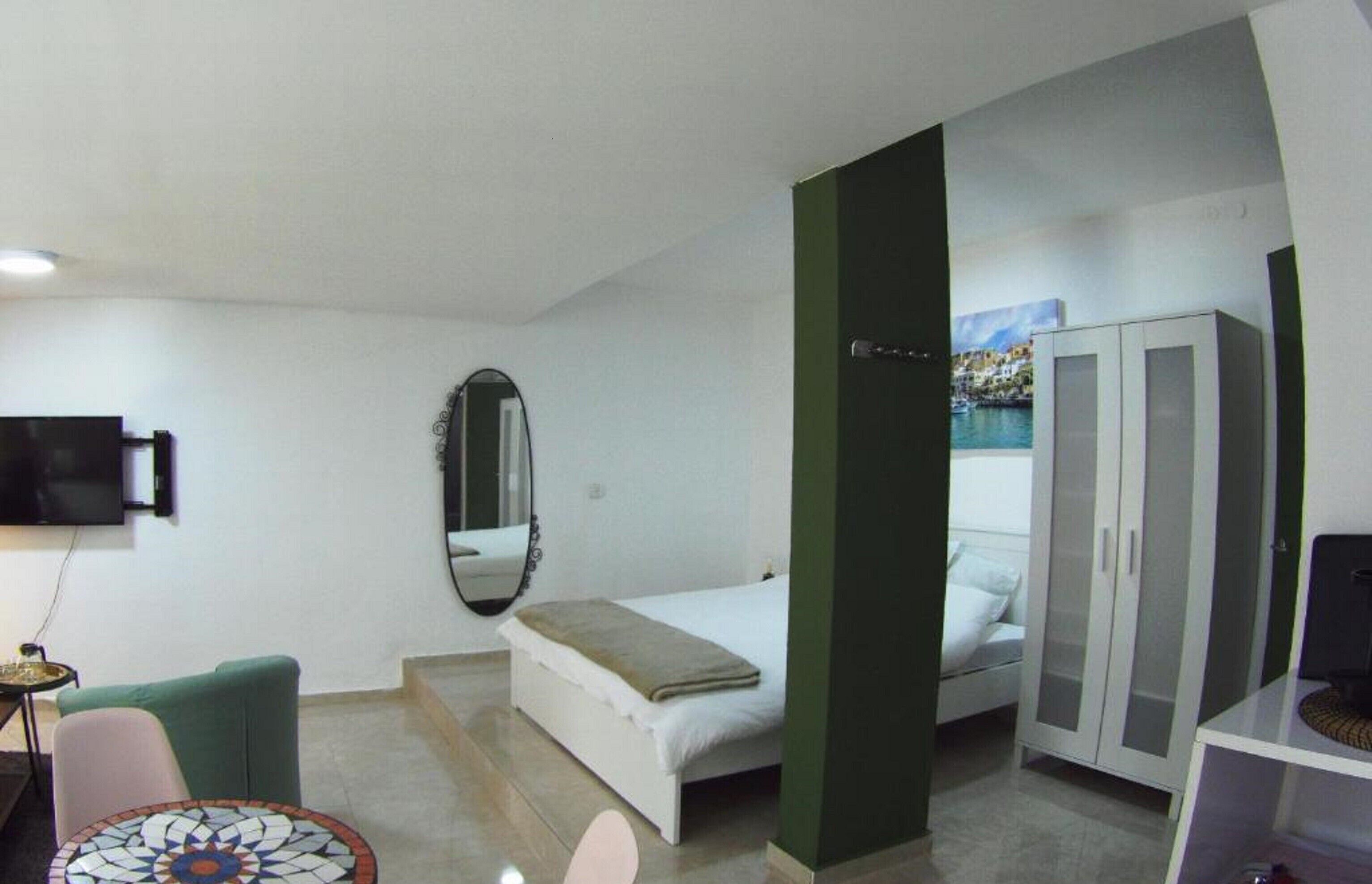 Habitación de hotel pequeña con cama, un espacio de descanso, televisión, armario y un cuadro en la pared.