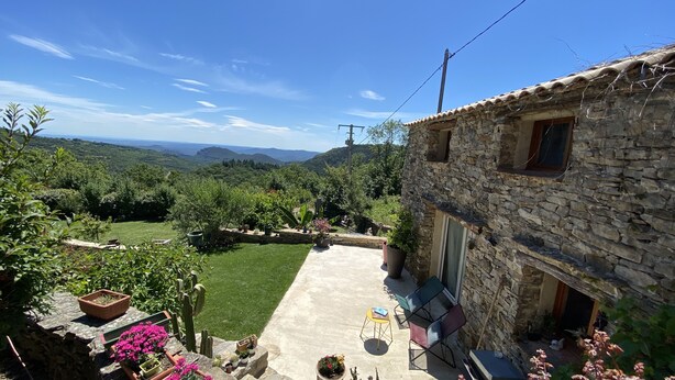 A stone building with a patio, surrounded by greenery and a view of distant hills. - Welcoming house, exceptional view, in the hamlet of Cezas. (Sumène)
