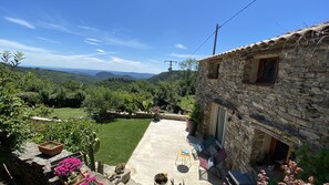 A stone building with a patio, outdoor seating, and a view of a green landscape with hills. - A welcoming home with exceptional views, located in the hamlet of Cezas. (Sumène)