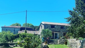 A stone house with a tiled roof, surrounded by a grassy yard and trees. - Welcoming house, exceptional view, in the hamlet of Cezas. (Sumène)