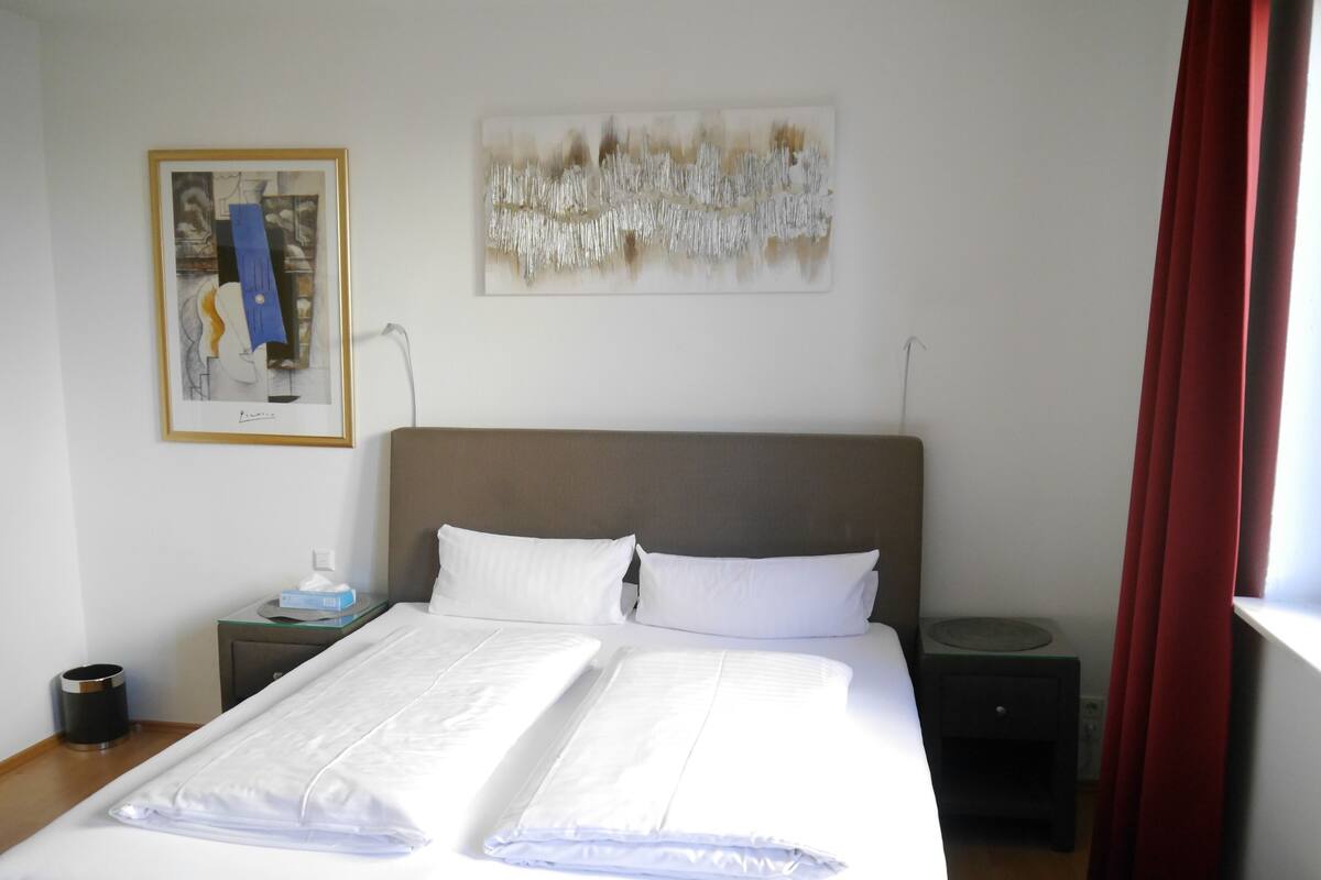 Un lit bien fait, avec du linge de lit blanc, une tête de lit marron et deux tables de chevet avec des lampes.