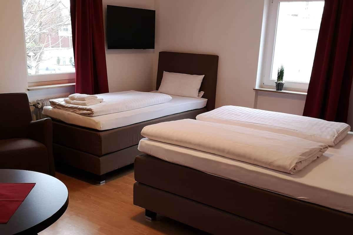 Une chambre d’hôtel avec deux lits, un téléviseur fixé au mur, une petite table avec une chaise et une fenêtre avec des rideaux.