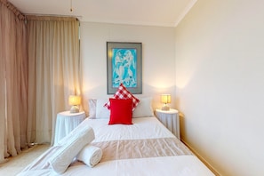 Une chambre d’hôtel avec un grand lit, deux tables de chevet avec des lampes, une œuvre d’art encadrée au mur et une fenêtre avec des rideaux.