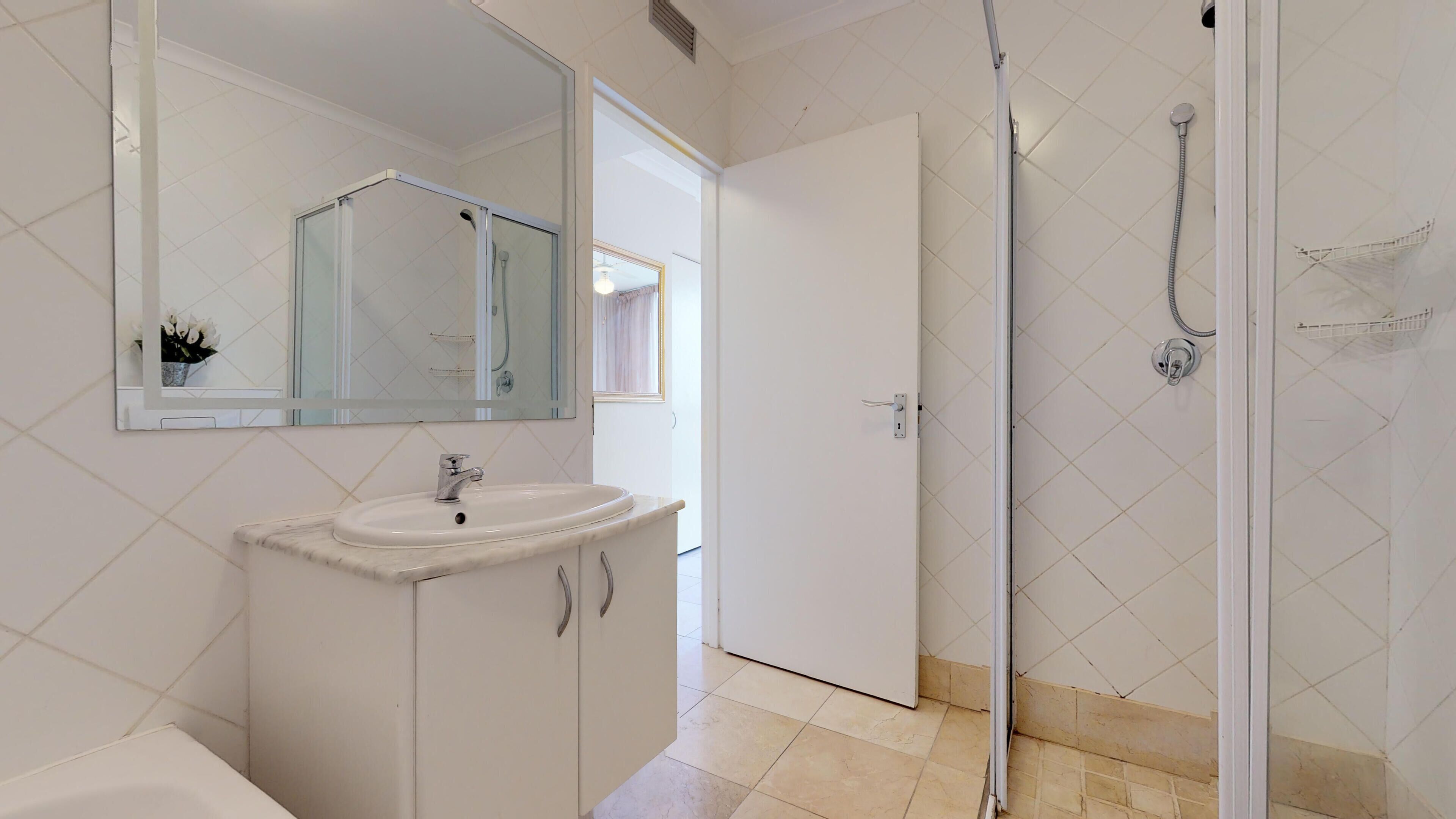 A bathroom with a white sink, mirror, and shower.
