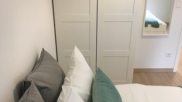 A bed with pillows in a room with a white wardrobe and a small mirror on the wall.
