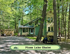 A two-story chalet with a porch, surrounded by trees, and labeled "Pines Lake Chalet". - Summer Fun in the Lake! Hot Tub, Golf Cart, Fire Pit, Family Memories! (Pocono Lake)