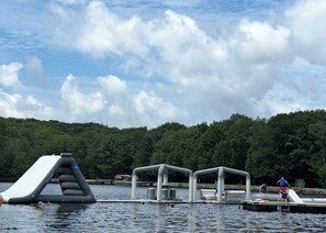 A water park with inflatable slides and platforms, surrounded by a forested area. - Summer Fun in the Mountains! Hot Tub, Golf Cart, Fire Pit, Family Memories! (Pocono Lake)