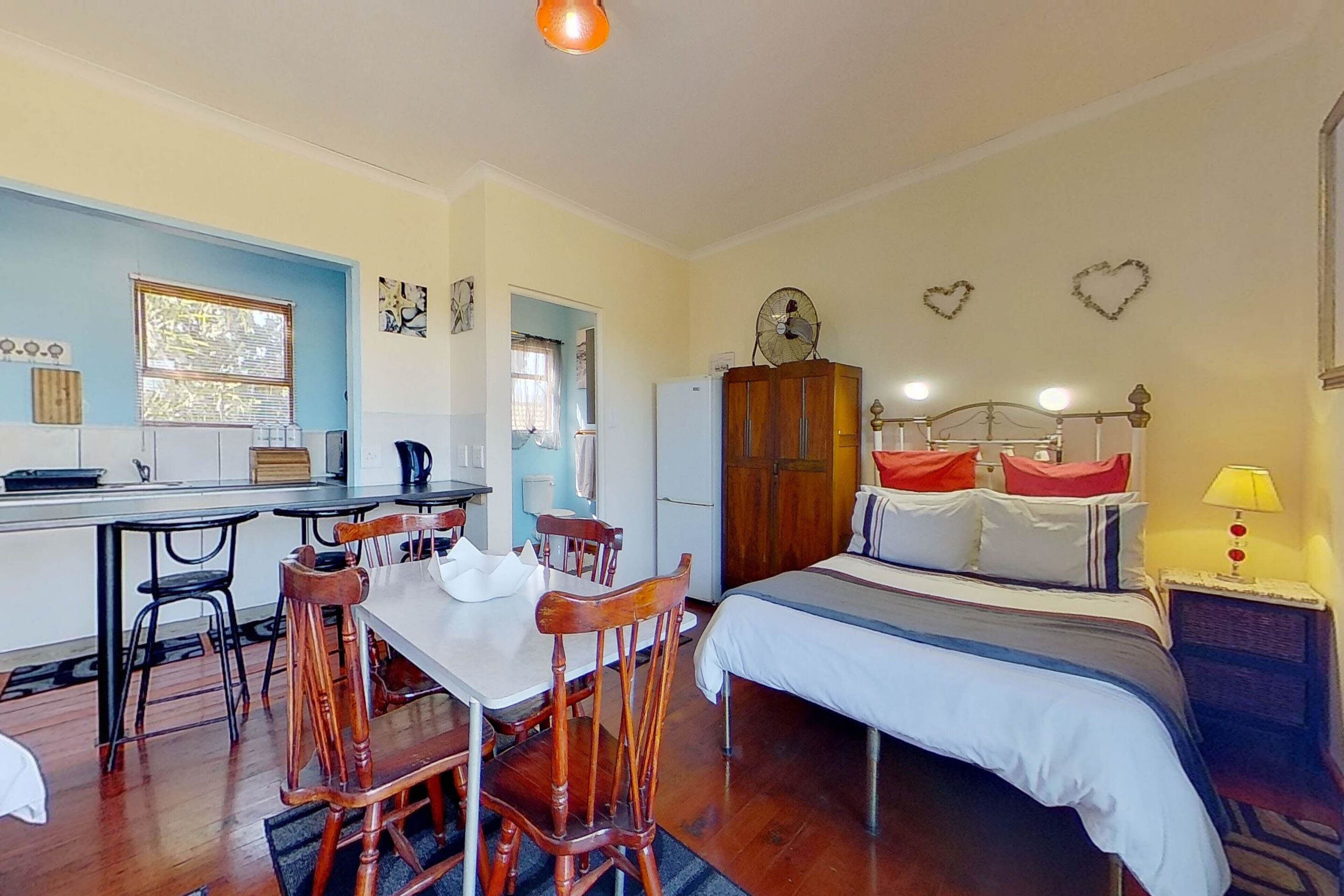 A compact room with a bed, a dining table with chairs, a kitchenette, and a small window.