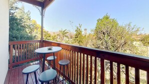 Ein Holzbalkon mit Tisch und vier Hocker, mit Blick auf eine Landschaft mit Bäumen und einem entfernten Turm.