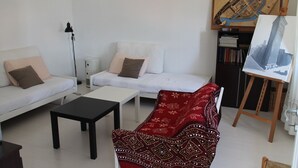 Una sala de estar con un sofá blanco, un sofá rojo estampado, una mesa de centro negra y un cuadro sobre un caballete.