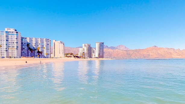 A coastal cityscape with modern high-rise buildings, a sandy beach, and mountains in the background. - Somerset Oaks (Cape Town)