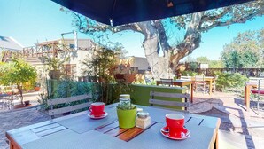 An outdoor patio with a table set for two, surrounded by potted plants and a large tree. - Somerset Oaks (Cape Town)