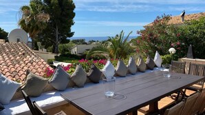 A terrace with a table and chairs, a view of the sea, and a tiled roof.
