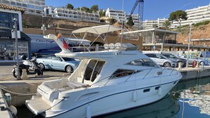 A marina with a white yacht docked at the pier, surrounded by other boats and a few cars.