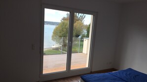 A bedroom with a large sliding glass door leading to a balcony with a view of a lake and trees. - Direct lake with large south-west balcony (new building 2019) (Überlingen)