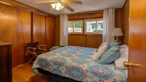 A bedroom with a wooden ceiling, a ceiling fan, a bed with patterned bedding, a chair, and a window with curtains. - SUPERB VIEW BIG  SEBAGO LAKE WESTERN SIDE OF LAKE (Standish)