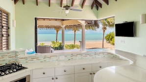 Una cocina con vista a la playa, un ventilador de techo y un televisor montado en la pared.